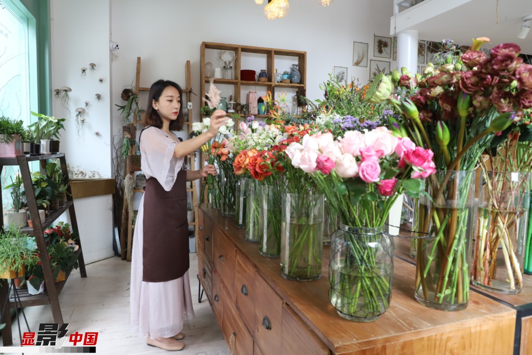 王黎媛是一名河南姑娘，在昆明念完大學后，就再也舍不下春城的藍天陽光、青山碧水，更舍不下這里的四時繁花，于是就干脆留了下來，成了一名媒體人。2017年的時候又毅然辭去工作，創(chuàng)業(yè)開起了花店，成了都市里的一名“花房姑娘”。圖為王黎媛在自己的花店中整理鮮花。新華網(wǎng) 周亞平/攝 念新洪/文